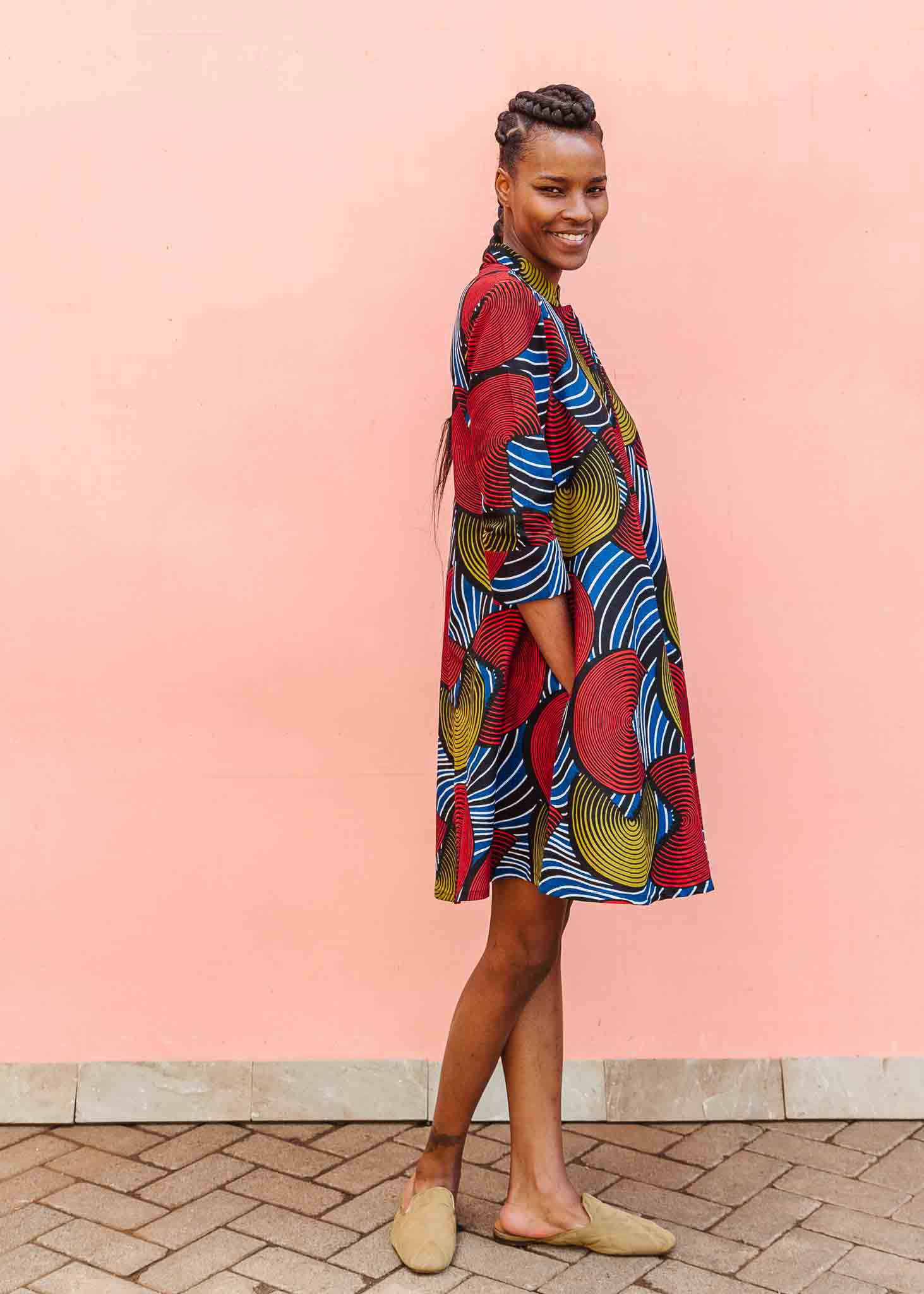 Model wearing circle design dress, featuring primary colors, paired with tan flats.