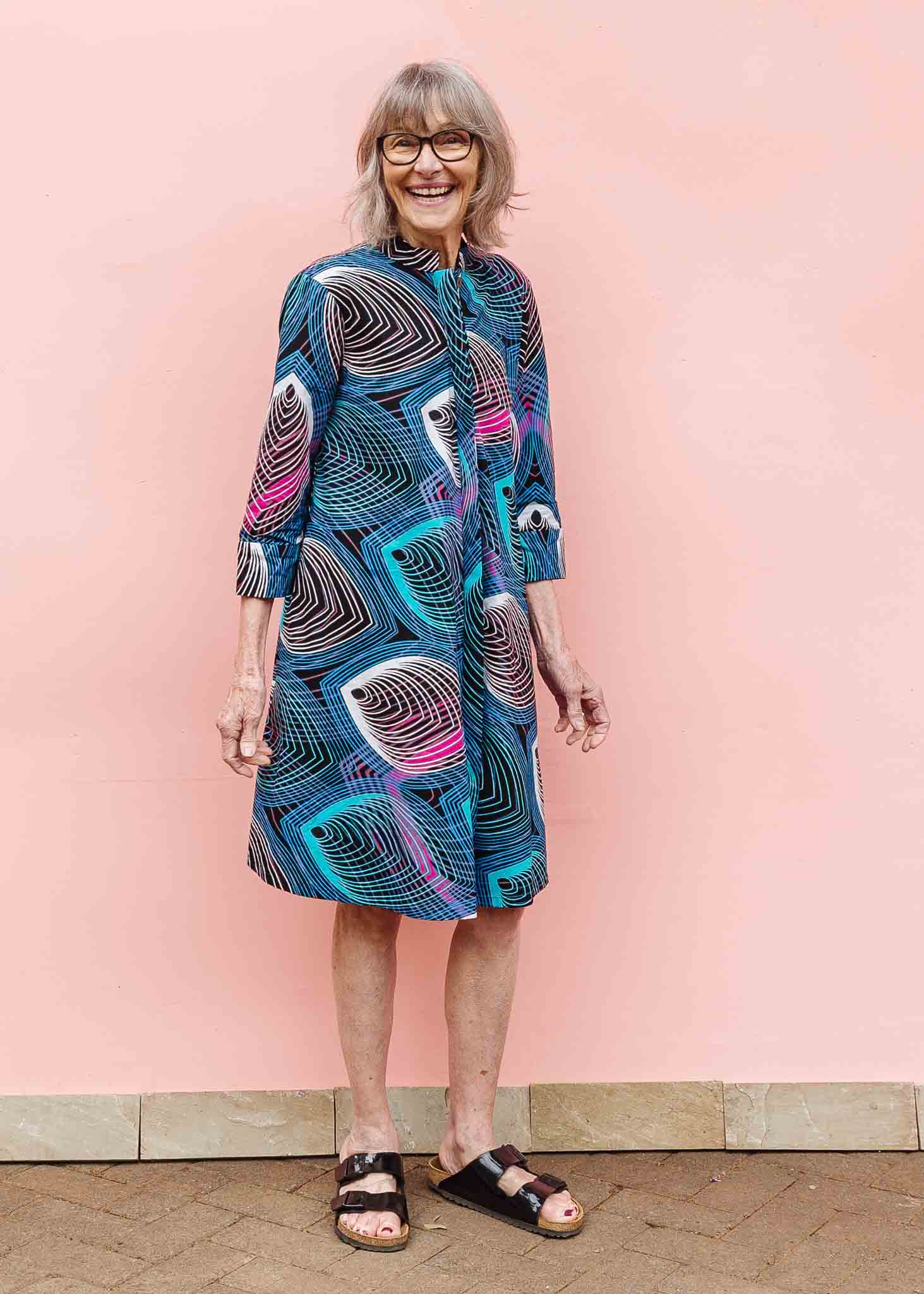 Model wearing black dress with colorful peacock print.