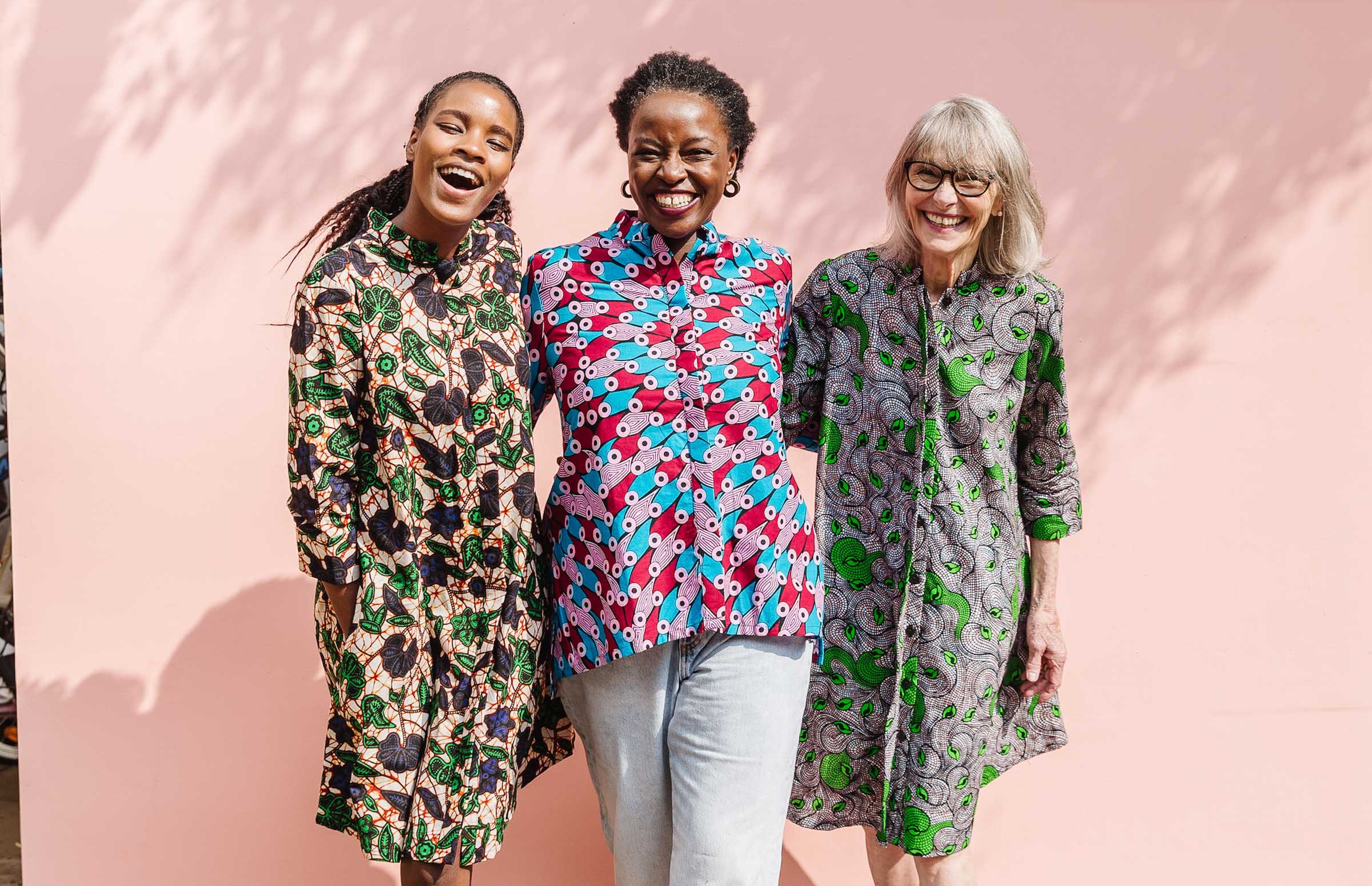 three women smiling arm in arm wearing multicolored clothing