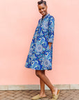 Model wearing blue paisley dress, paired with tan flats.