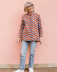 Model wearing blue and red zigzag print long sleeved blouse, paired with jeans and white sneakers.