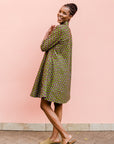 Model wearing green dress with small purple fowl print, paired with beige flats.