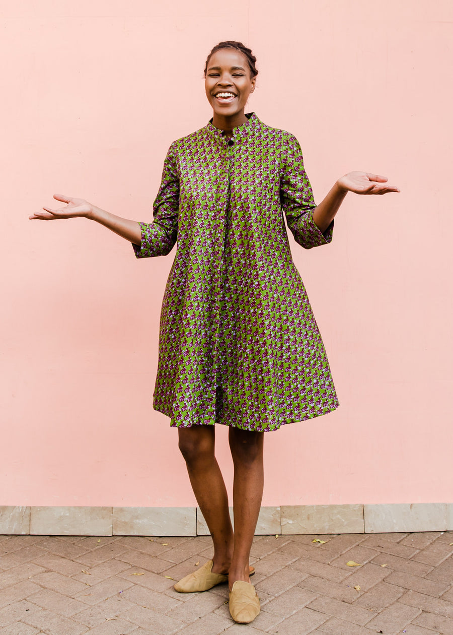Model wearing green dress with small purple fowl print, paired with beige flats.