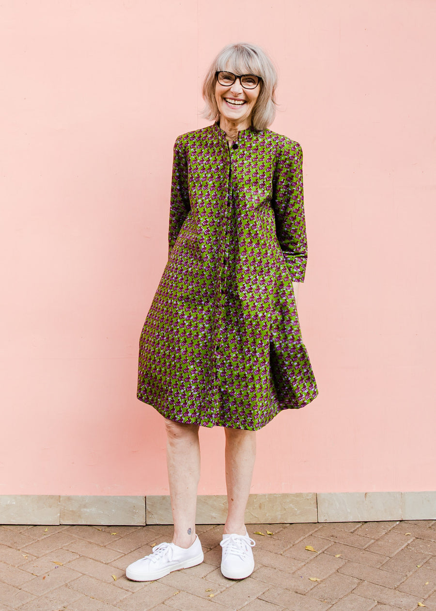 Model wearing green dress with small purple fowl print, paired with white sneakers..