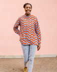 Model wearing blue and red zig zag print long sleeved blouse, paired with jeans and tan flats.